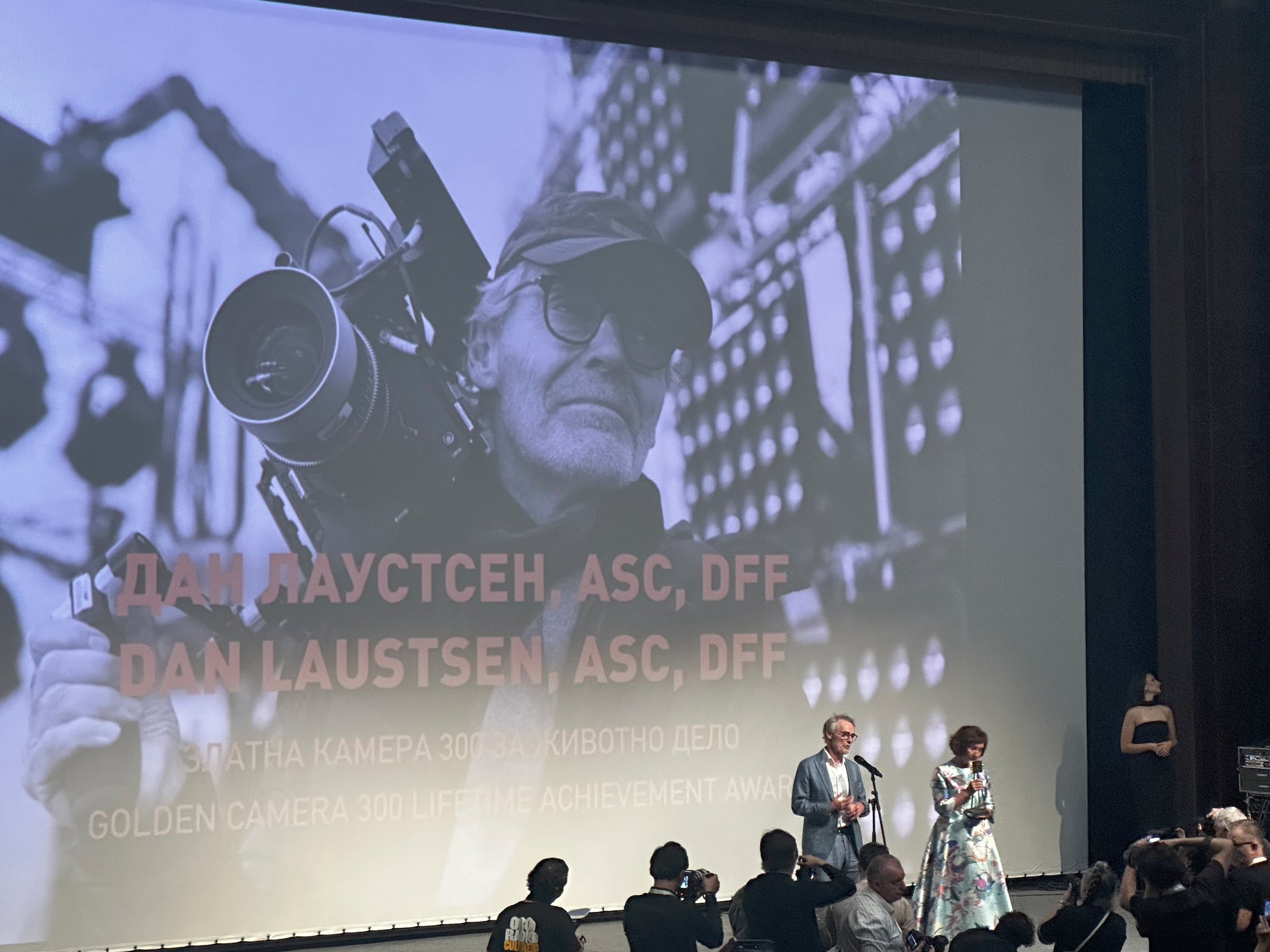 Dan Laustsen sur scène, recevant sa Golden Camera 300 devant son portrait projeté sur l’écran