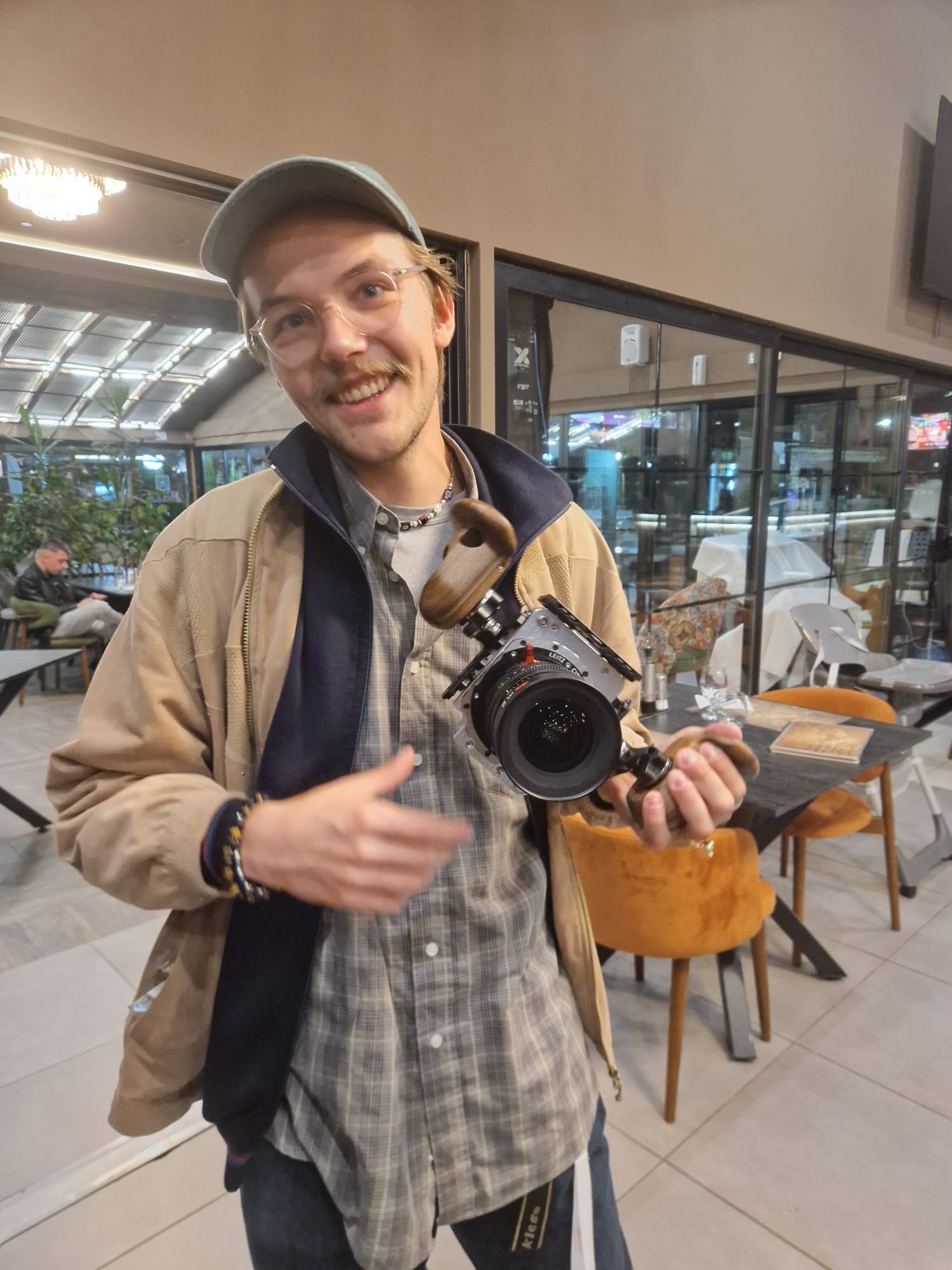 Yvan Rodionov, souriant, une caméra de cinéma à poignées en bois entre les mains, dans la salle du dîner des fabricants